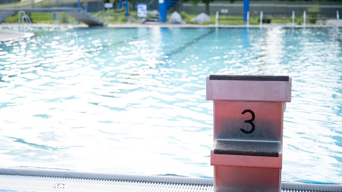 Ein Schwimmbecken mit klarem Wasser und einer Rutsche im Hintergrund. Am Beckenrand steht eine Startblatte mit der Nummer drei. | © Schilcherland Steiermark