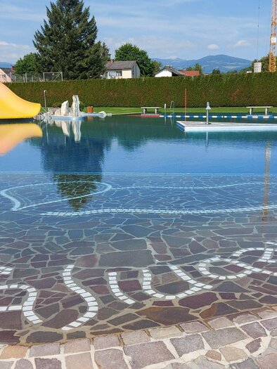 Ein großzügiges Schwimmbad mit einem Rutschenbereich und klarem Wasser. Umgeben von grünen Bäumen und einem blauen Himmel. | © Stadtgemeinde Voitsberg - Mayer