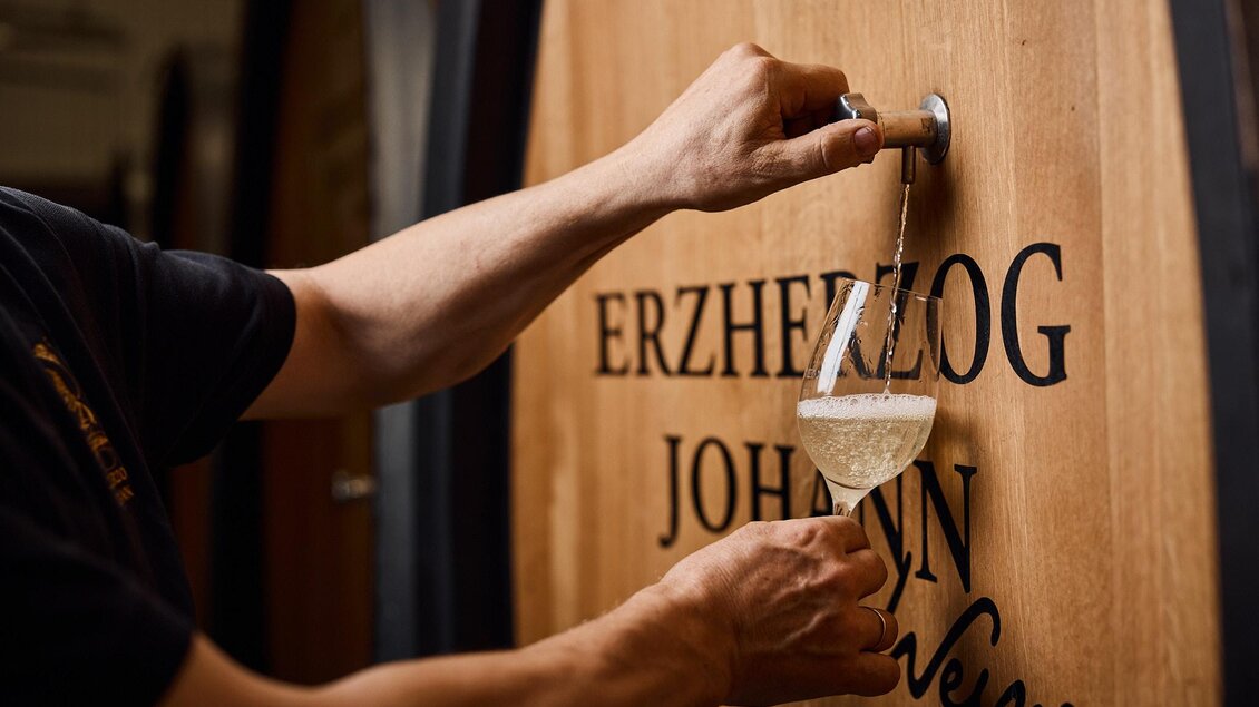 Ein Winzer zieht Wein aus einem Holzfass. Im Vordergrund sieht man ein Glas, das mit dem weißen Wein gefüllt wird. | © Erzherzog Johann Weine