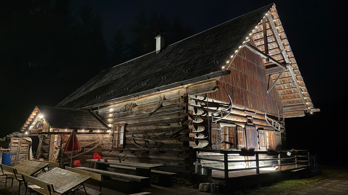 Eine gemütliche Holzhütte, die nachts beleuchtet ist. Im Vordergrund sind Tische und Bänke zu sehen. | © Eselalm