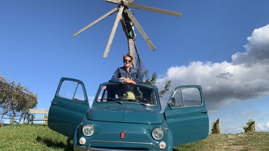 Ein grüner Kleinwagen steht auf einer Wiese mit offenen Türen. Im Hintergrund ist ein Windrad und ein blauer Himmel zu sehen. | © Event Mobile