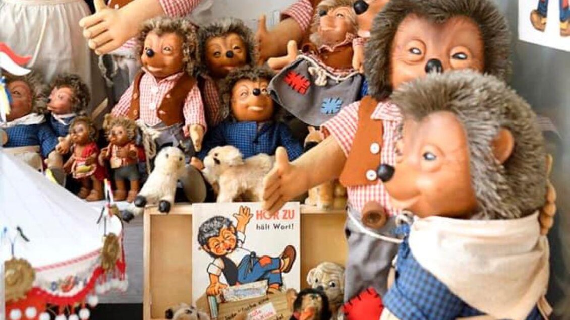 Eine Sammlung von Stofftieren und Puppen in bunten Outfits, die tierähnliche Merkmale haben. Im Hintergrund sind Bilder und ein Buch mit Geschichten zu sehen. | © Eva Kohlbacher