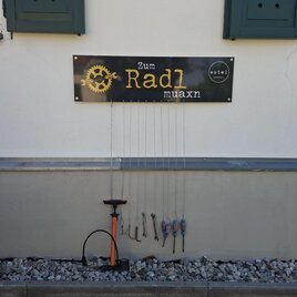 <p>Ein Schild mit der Aufschrift "Zum Radl maaxn" hängt an einer Wand. Darunter sind verschiedene Werkzeuge und eine Luftpumpe für Fahrräder angebracht.Wotel in Söchau</p> | © Wotel Söchau