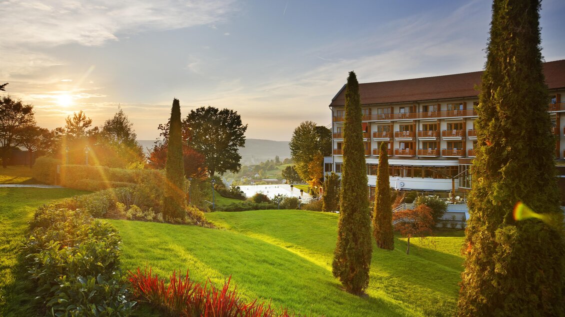 Ein malerisches Hotel inmitten von gepflegten Gärten und Bäumen. Die Sonne geht unter und schafft eine entspannende Atmosphäre. | © Der Steirerhof