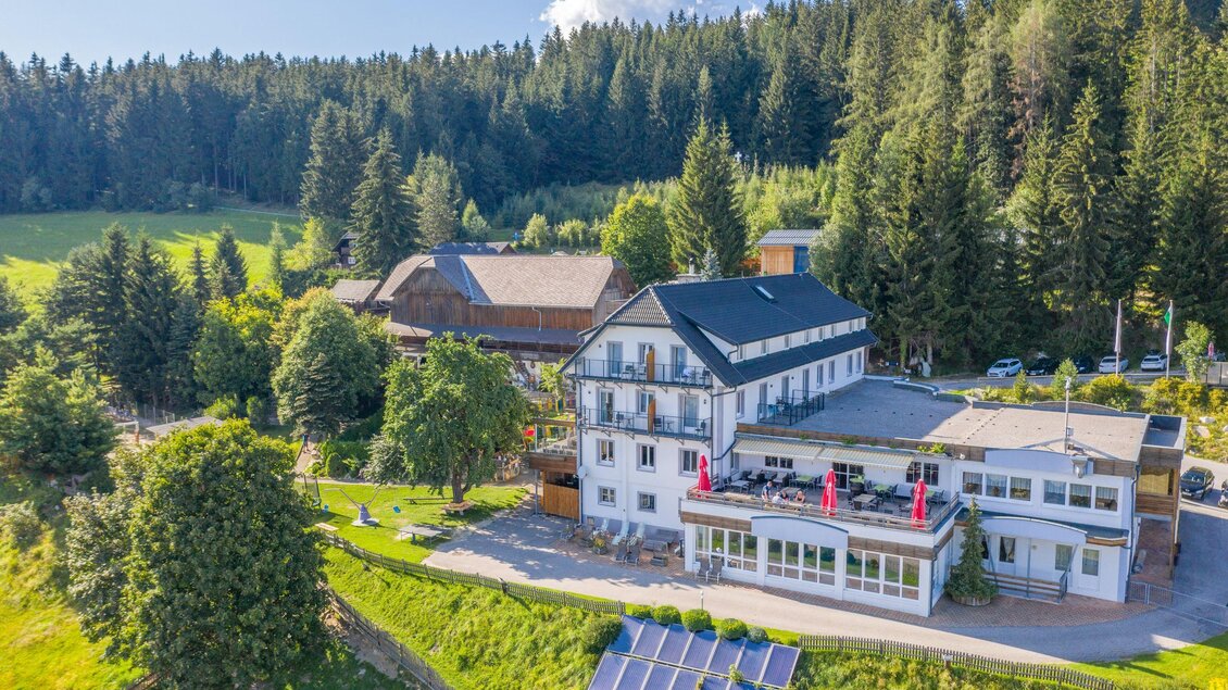 Ein malerisches Hotel inmitten grüner Wälder und sanfter Hügel. Auf dem Gelände sind Solarpanels und gepflegte Gärten sichtbar. | © Familienhotel Berger