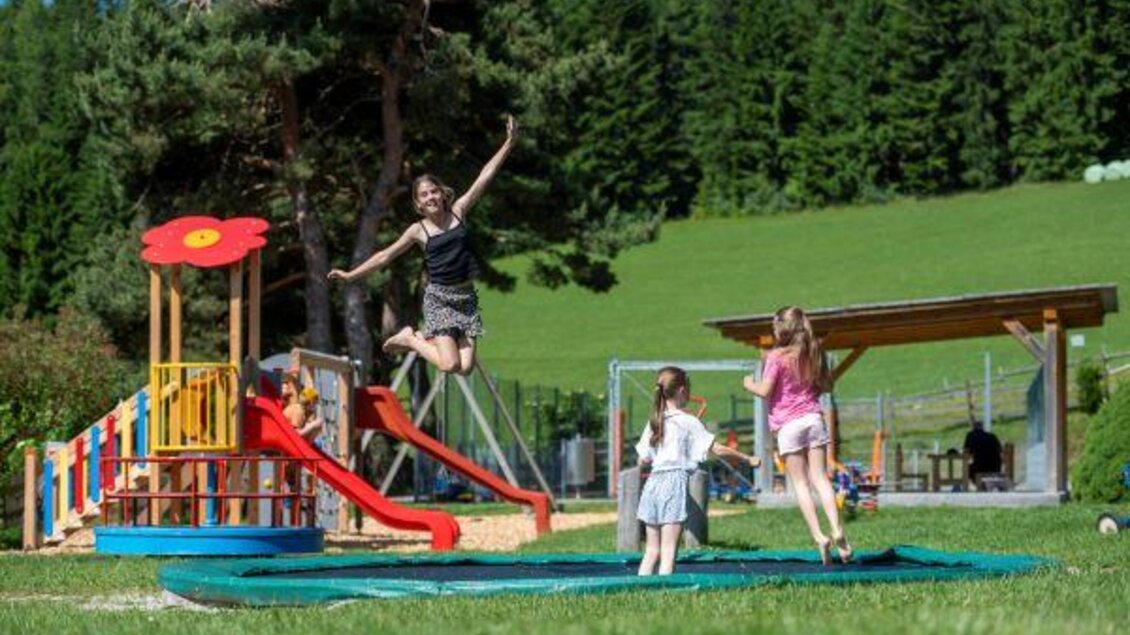 Eine Mutter spielt mit ihrer Tochter auf einem Spielplatz. Im Hintergrund sind Rutschen und ein Spielturm zu sehen. | © Familienhotel Berger