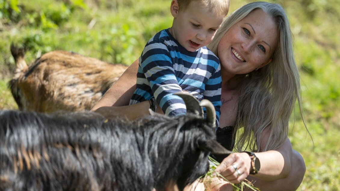 Zu sehen ist eine Mutter mit Kind die eine Ziege streicheln. | © Familienhotel Berger