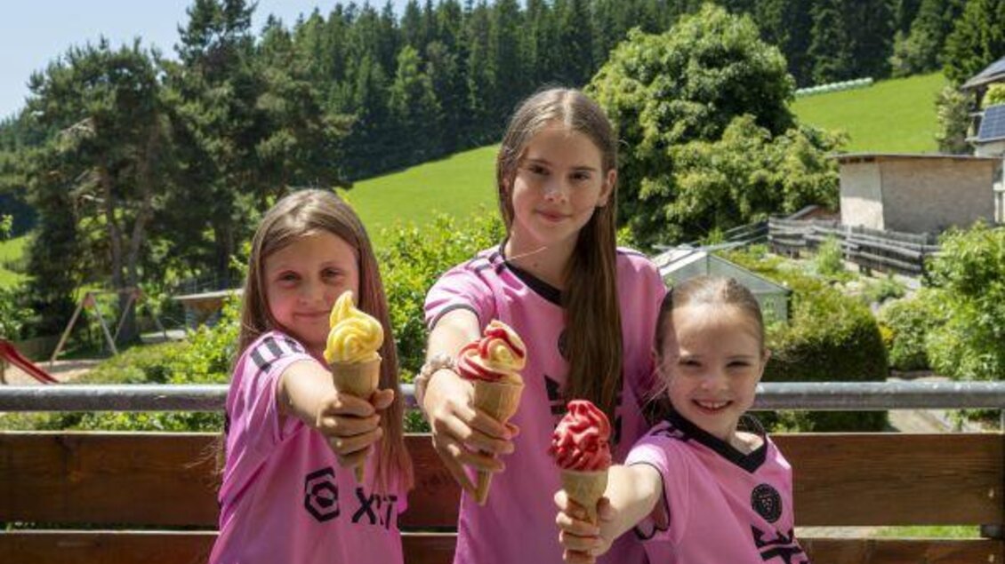 Zu sehen sind 3 Mädchen in rosa T-Shirts mit einem Stanizel Softeis in der Natur. | © Familienhotel Berger