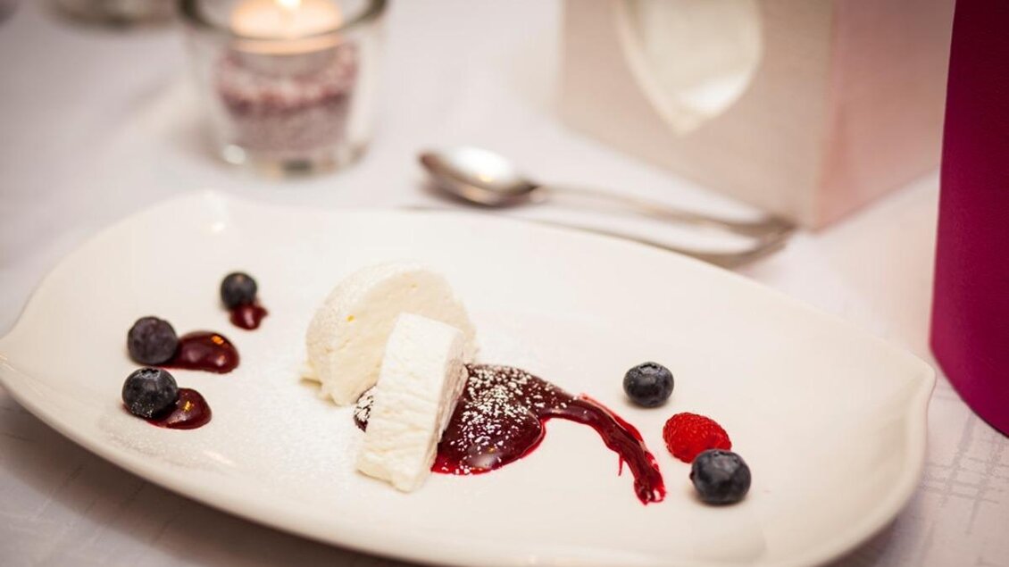 Ein elegantes Dessert auf einem weißen Teller. Es besteht aus Eiscreme, Beeren und einer fruchtigen Sauce. | © Familienhotel Berger