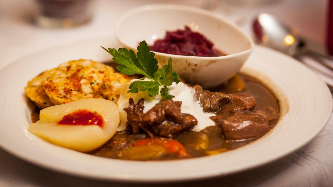 Ein ansprechender Teller mit einem herzhaften Fleischgericht, Kartoffelknödeln und roter Beete. Ein frisches Blatt Petersilie garnisiert das Gericht. | © Familienhotel Berger