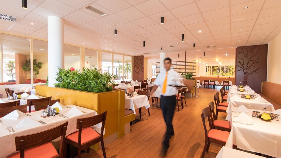 Ein modernes Restaurant mit eleganten Tischen und Holzfußboden. Ein Kellner serviert den Gästen in einem hellen und freundlichen Ambiente. | © Eisenberger