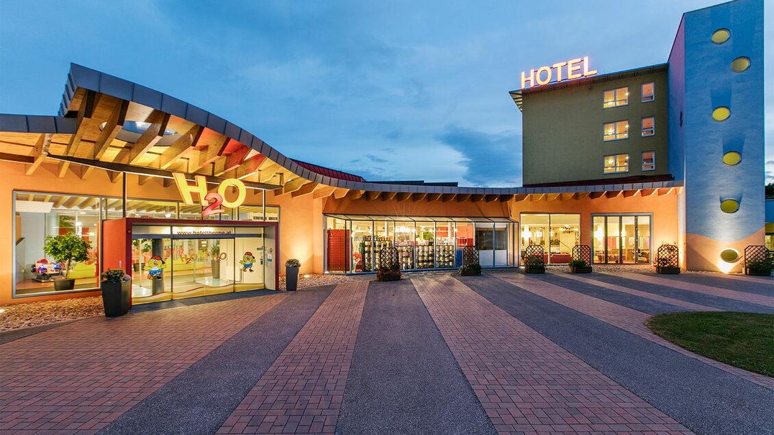 Ein modernes Hotel mit einer einladenden Fassade und beleuchteten Schildern. Der Außenbereich ist gepflastert und gut gestaltet. | © Eisenberger