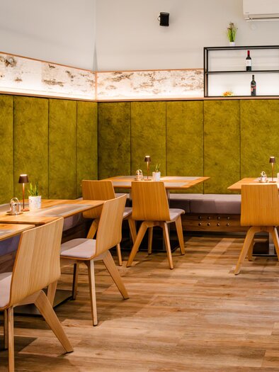 Modern dining area in Feldkirchnerhof with wooden tables, chairs, and green wall paneling | © Region Graz - Mias Photoart