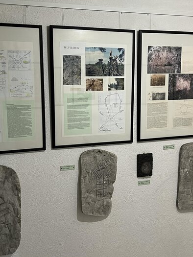 Eine Ausstellung mit mehreren gerahmten Bildern und Informationen an der Wand, darunter verschiedene Steintafeln. Die Tafeln zeigen alte Inschriften und Zeichnungen. | © Felsenbildmuseum - Steinmuseum