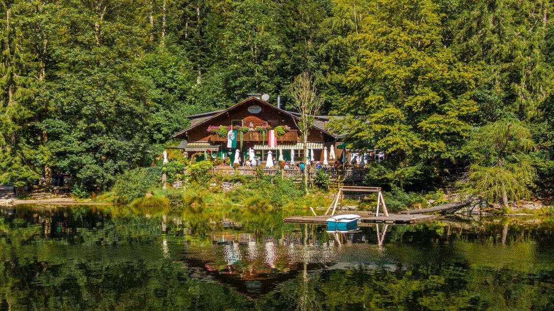 Ein malerisches Restaurant am Wasser, umgeben von Bäumen. Die Spiegelung im ruhigen See schafft eine friedliche Atmosphäre. | © Andreas Syen
