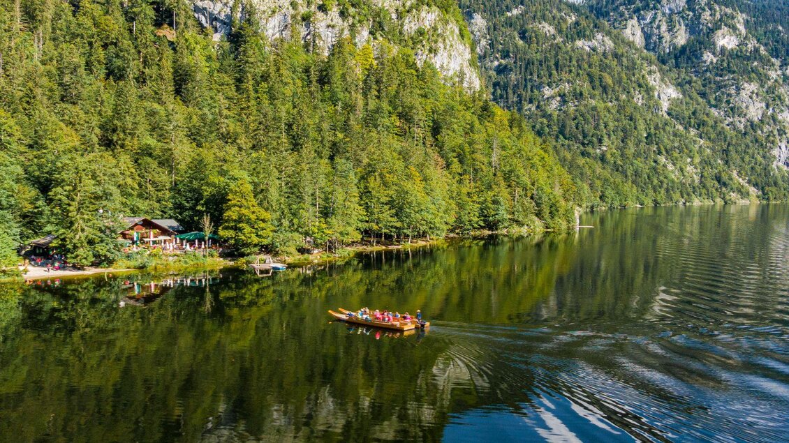 Ein ruhiger See umgeben von grünen Wäldern und Bergen. Ein Boot fährt sanft über die spiegelnde Wasseroberfläche. | © Andreas Syen