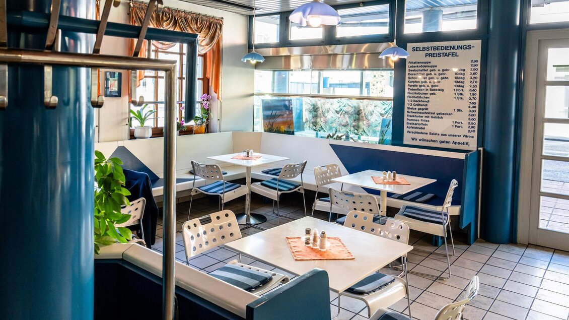 Ein gemütliches Restaurant mit weißen Tischen und Stühlen. Große Fenster sorgen für viel Licht und eine einladende Atmosphäre. | © Stephan Friesinger