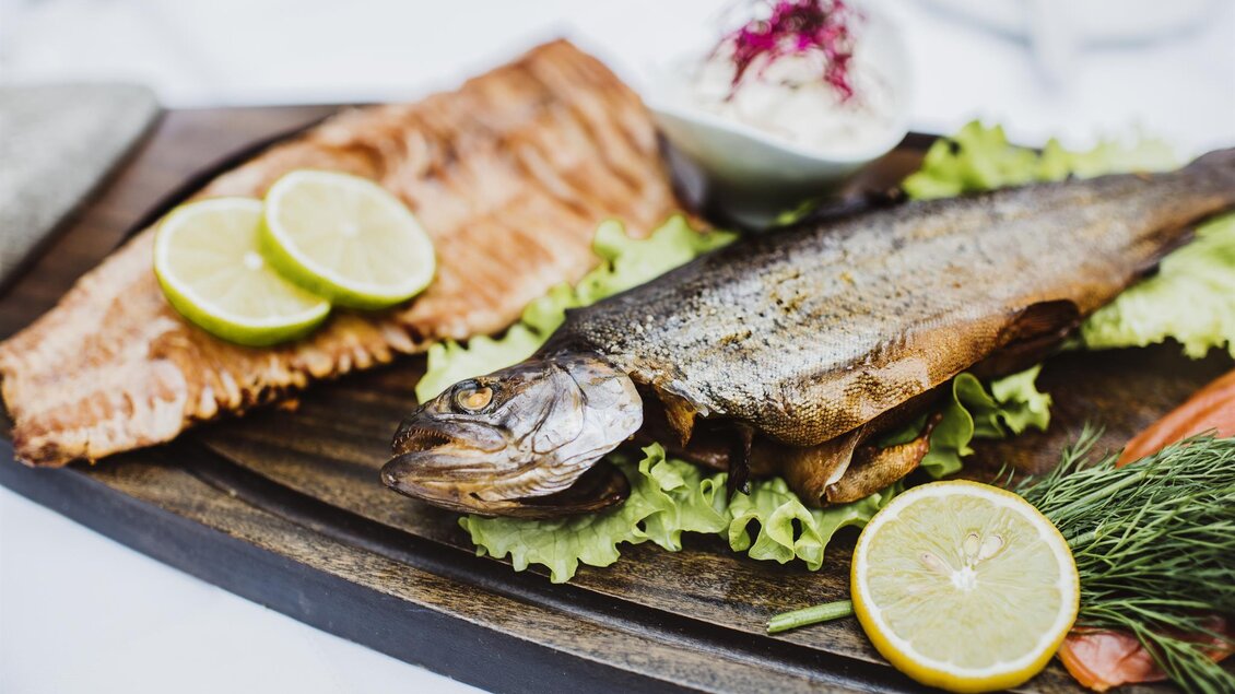 Ein frisch zubereitetes Fischgericht auf einem Holzbrett. Dazu gibt es Zitronen und eine Beilage aus Salat und Sauerrahm. | © Fischrestaurant Kulmer