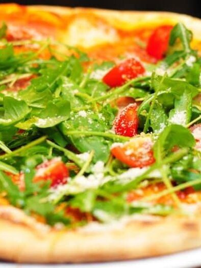 A freshly baked pizza with ham, arugula, and cherry tomatoes. The crust is crispy and golden brown. | © Food Mama