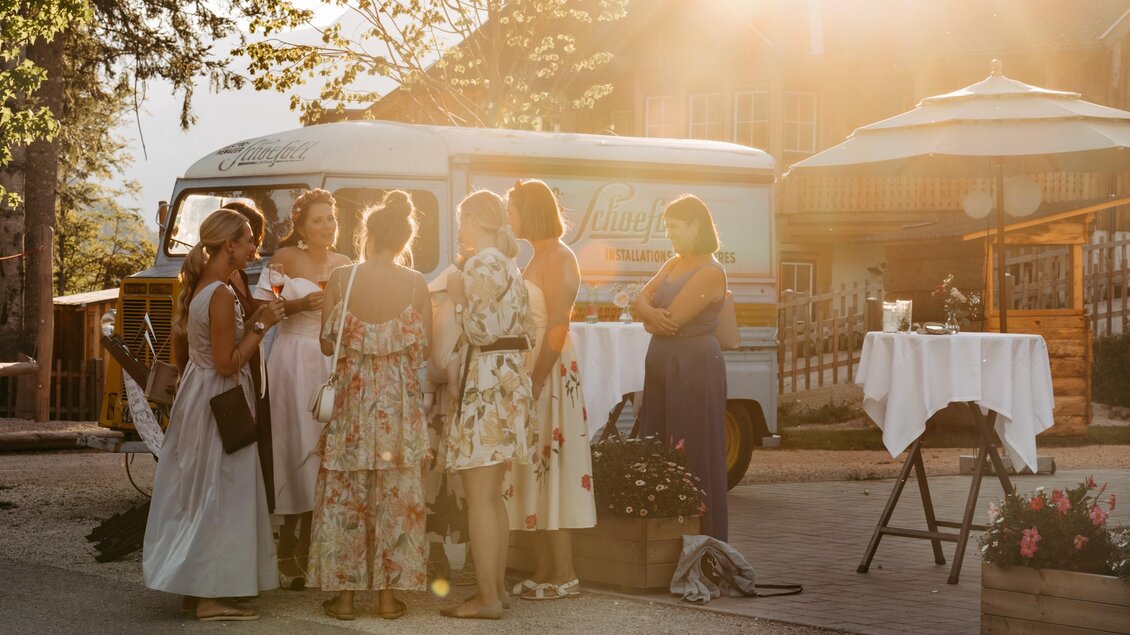 Eine Gruppe von Frauen in schönen Kleidern steht zusammen bei einem Event im Freien. Die Szenerie wird von warmem Licht und einer gemütlichen Atmosphäre geprägt. | © Narzissendorf Zloam www.zloam.at