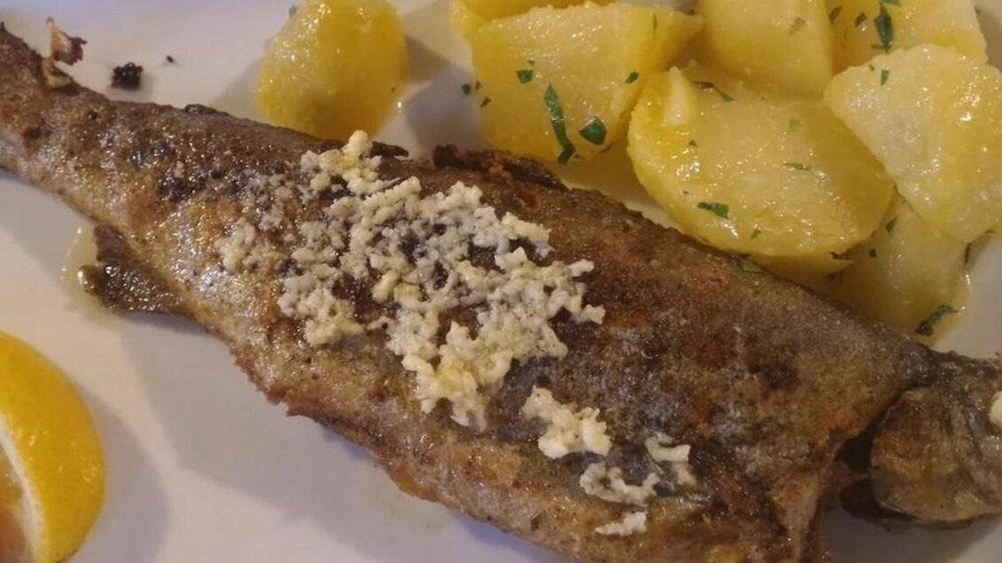 Ein gebratener Fisch, garniert mit Butter, liegt auf einem Teller. Daneben befinden sich gekochte Kartoffeln und ein Stück Zitrone. | © Forellengasthof Falkenbauer