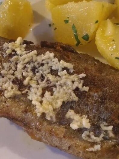 A fried fish, garnished with butter, lies on a plate. Next to it are boiled potatoes and a slice of lemon. | © Forellengasthof Falkenbauer