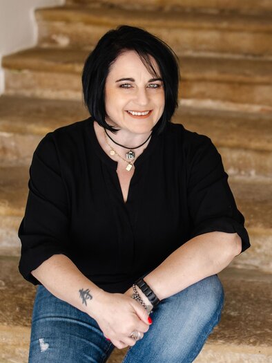 Eine Frau sitzt auf einer Treppe und lächelt freundlich. Sie trägt ein schwarzes Oberteil und Jeans. | © Karin Bergmann