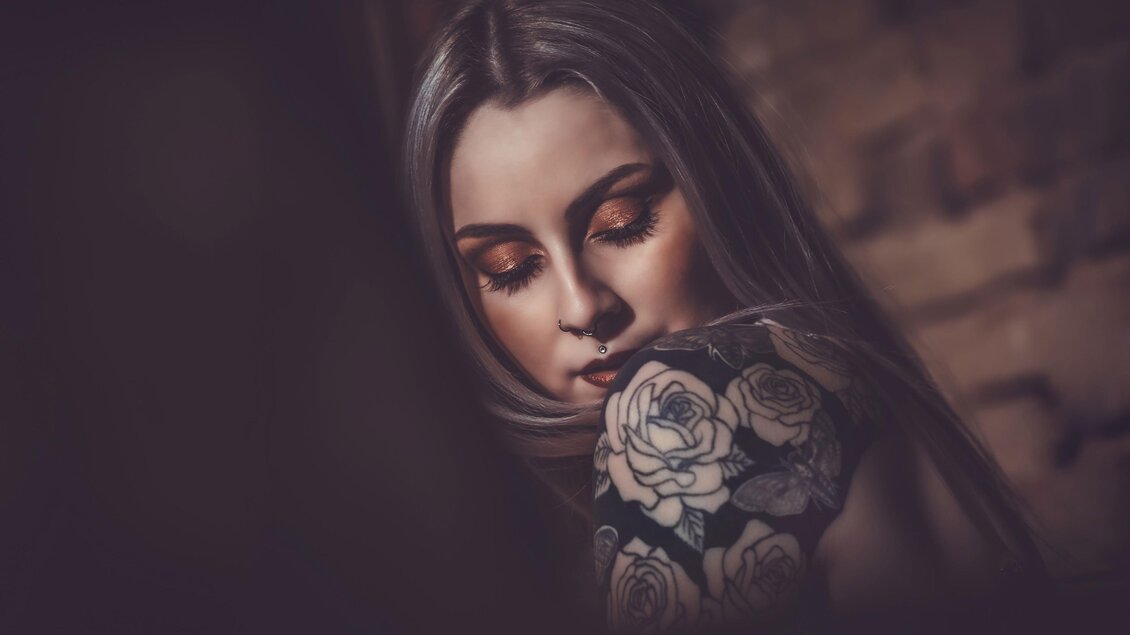 Eine Frau mit langen, grauen Haaren und auffälligem Make-up. Sie zeigt ein Tattoo von Rosen auf ihrem Arm. | © Nicole Oberhofer – FotoGrafin