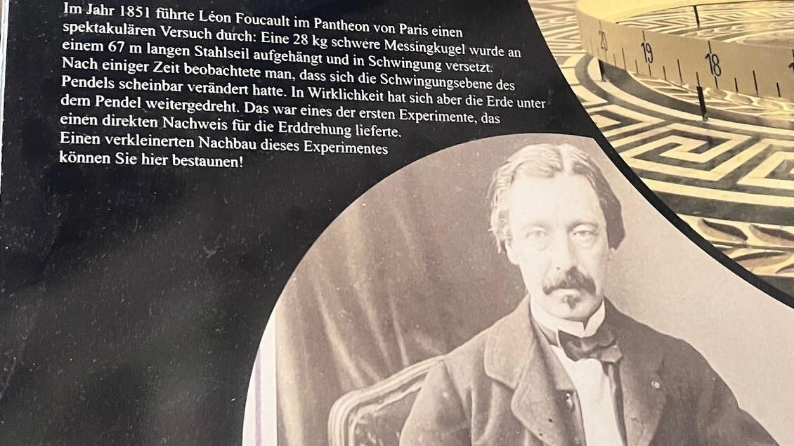 Ein Ausstellungsschild zum Foucaultschen Pendel, das die Erdrotation zeigt. Darunter ist ein historisches Porträt eines Mannes und Informationen über die Ausstellung. | © Tourismusverband Oststeiermark