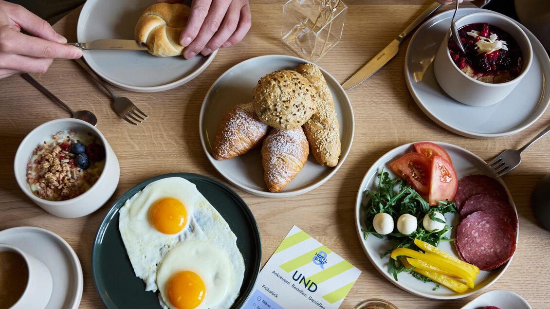 Ein gedeckter Tisch mit verschiedenen Frühstücksgerichten. Es gibt Eier, Obst, Gebäck und Getränke.