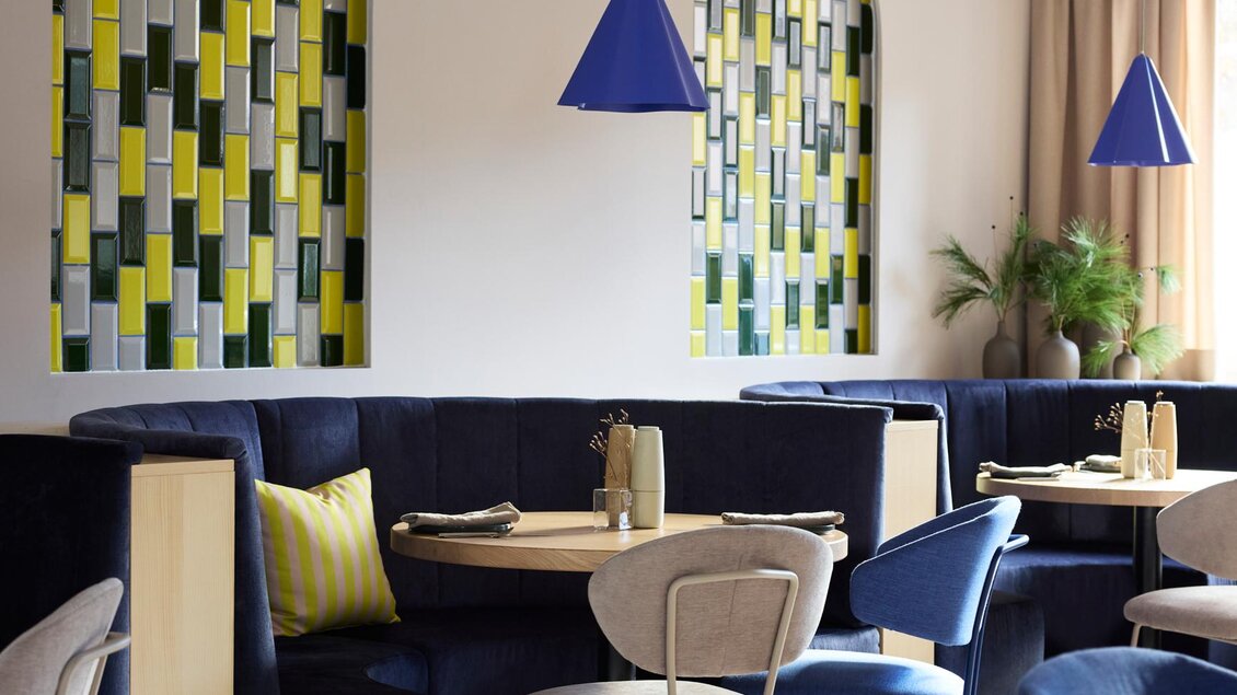 Ein modernes Restaurant mit bunten Wänden und stilvollen Sitzbereichen. Die Farbakzente in Gelb und Blau schaffen eine einladende Atmosphäre. | © @hotelund.me 
