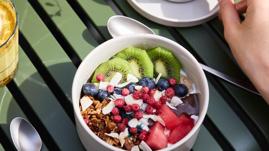 Eine Schüssel mit frischem Obst, Joghurt und Müsli liegt auf einem Tisch. Daneben steht eine Tasse Kaffee. | © @hotelund.me 