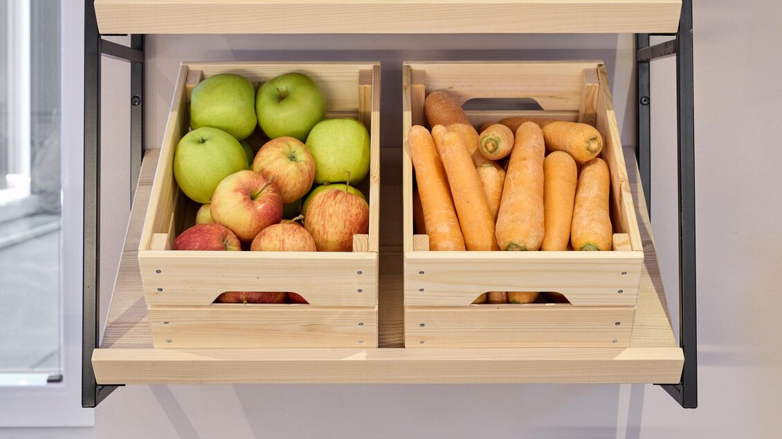 Frische Gemüse und Obst in Holzboxen stehen auf einem Regal. Auf einem Schnittbrett befindet sich ein Teller mit roten Beeten und ein Glas Saft. | © @hotelund.me 