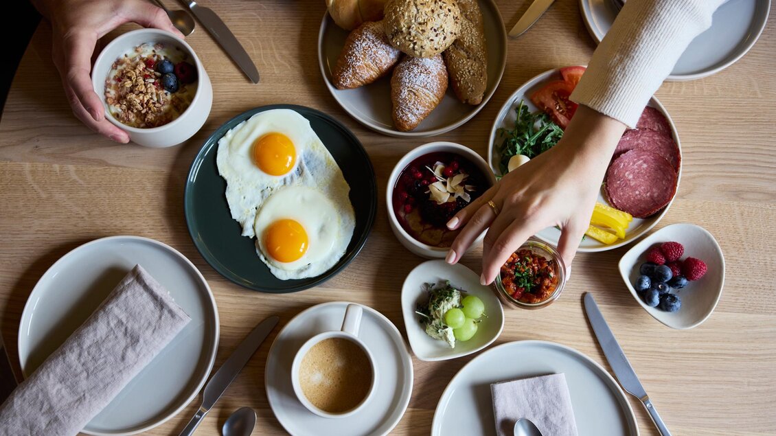 Ein reichhaltiges Frühstückstisch mit Eiern, frischen Brötchen, Salat und Früchten. Kaffee und Geschirr ergänzen die Mahlzeit. | © @hotelund.me 