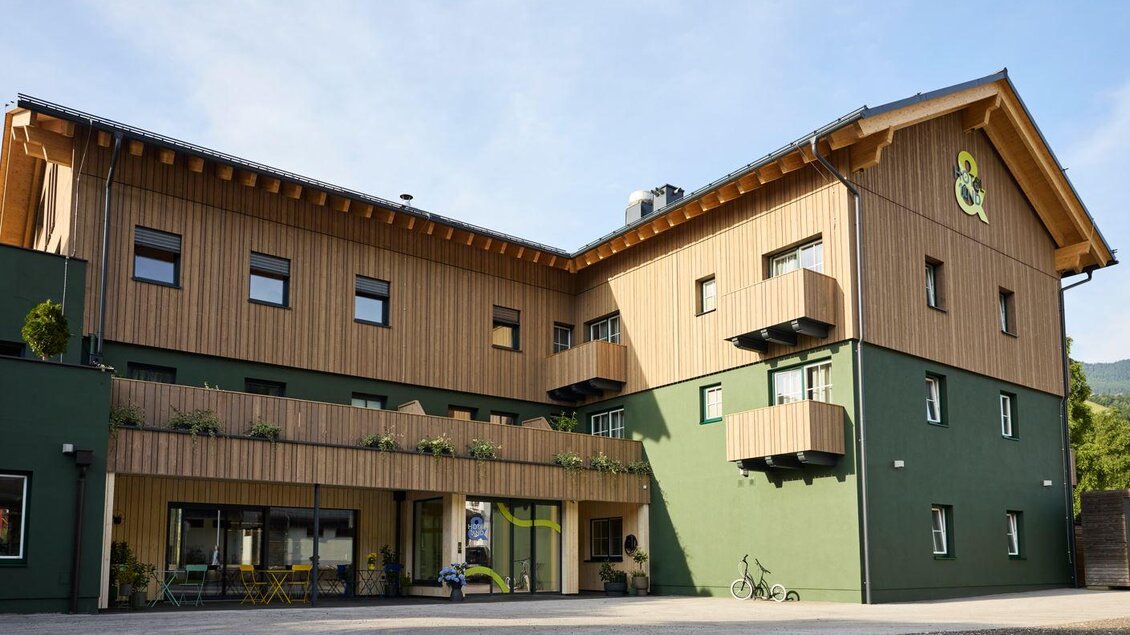 Ein modernes Gebäude mit Holzverkleidung und einer grünen Fassade. Es gibt Balkone und Fenster, die einladend wirken. | © @hotelund.me 