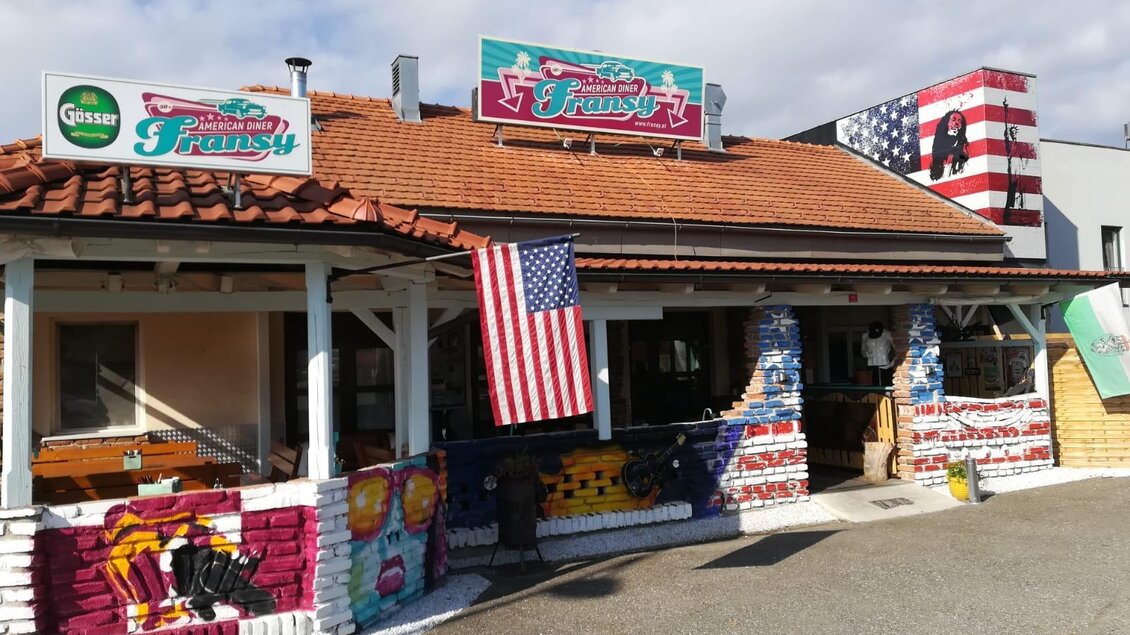 Ein buntes Restaurant mit amerikanischer Flagge und kreativer Wandmalerei. Der Außenbereich ist einladend und zeigt verschiedene farbige Motive. | © Fransy American Diner
