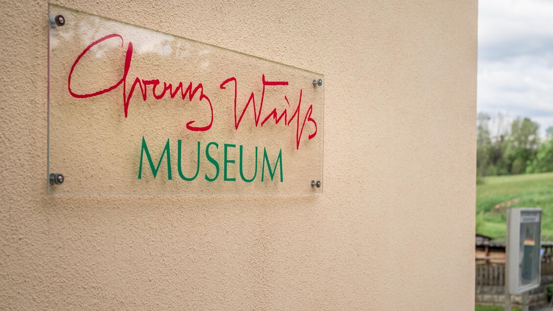 Schild des Franz Weiß Museums in Voitsberg mit roter Signatur und grünem Schriftzug an der Fassade | © TV Region Graz - Die Abbilderei