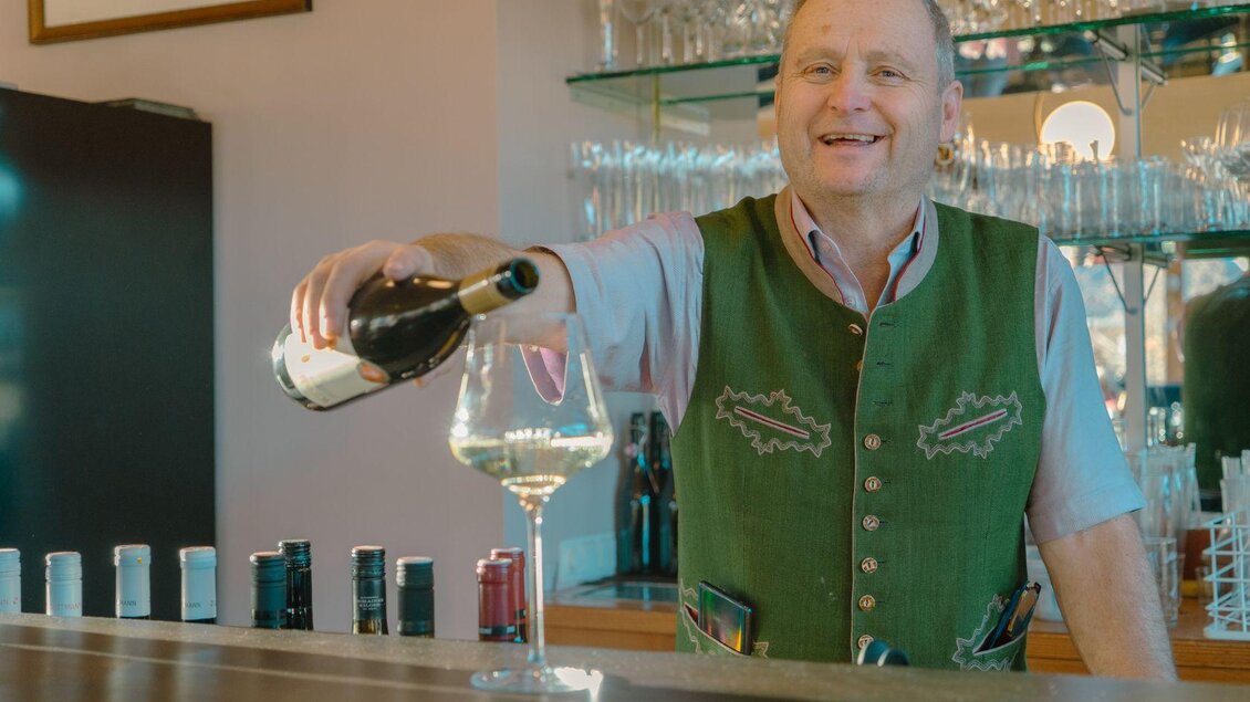 Der Gastwirt Franz bei der Arbeit. Er schenkt freudig ein Glas Weißwein an der Bar ein.  | © Elisabeth Pichler