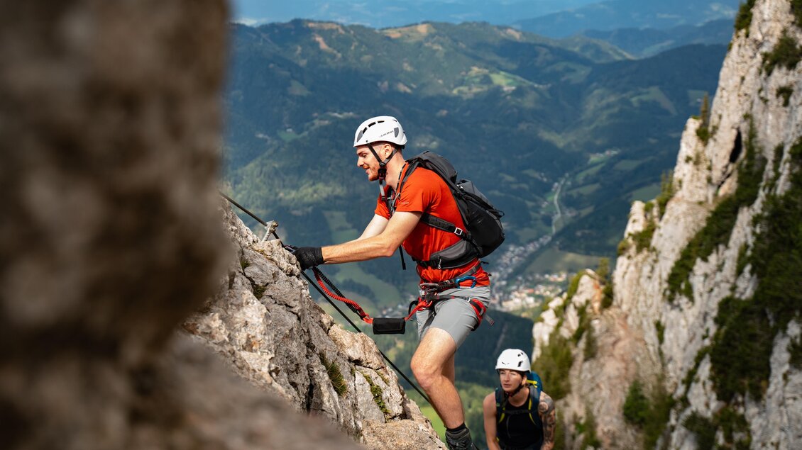 Zwei Kletterer erklimmen einen steilen Felsen in den Bergen. Im Hintergrund sind grüne Hügel und ein klarer Himmel zu sehen. | © Oststeiermark Tourismus