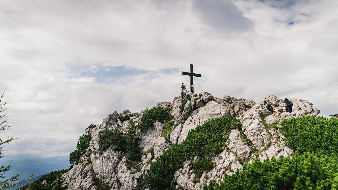 Ein majestätischer Berggipfel mit einem Kreuz und Wanderern. Im Hintergrund sind sanfte Hügel und ein klarer Himmel zu sehen. | © Oststeiermark Tourismus