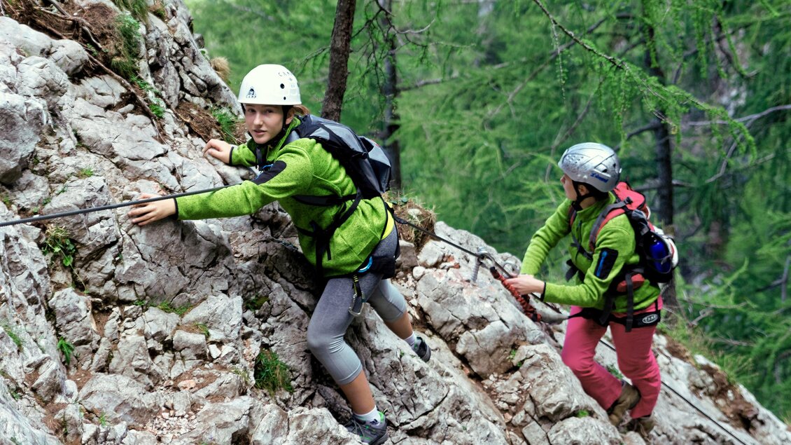 Zwei Kletterer erklimmen einen steilen Felsen in einer bewaldeten Berglandschaft. Sie tragen Helme und Kletterausrüstung. | © Tourismusverband Oststeiermark