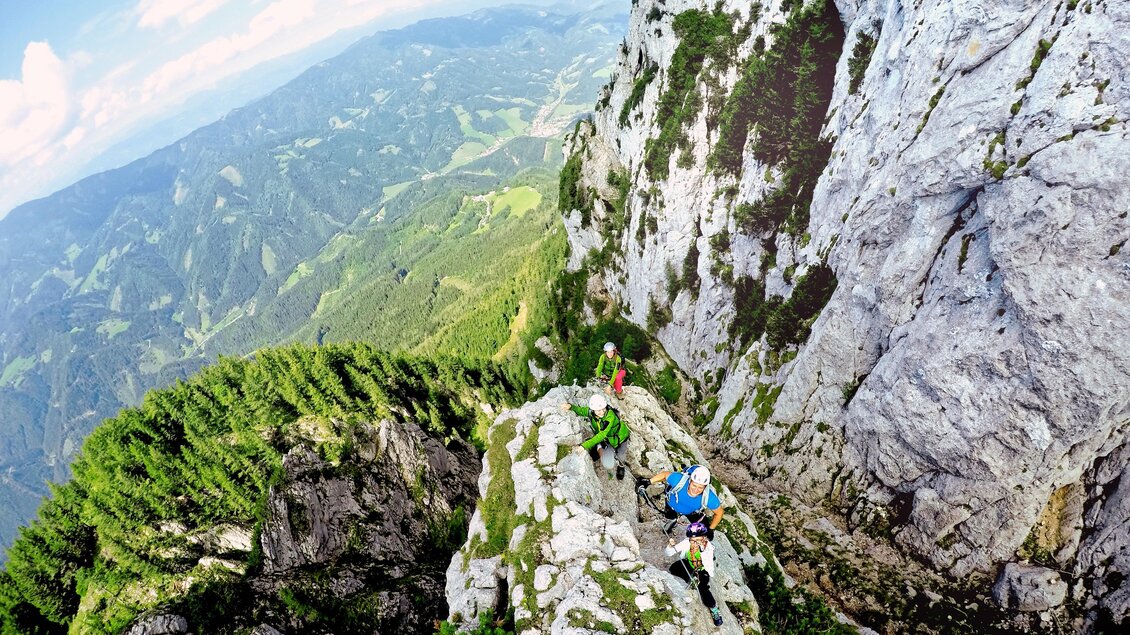 Eine Gruppe von Kletterern befindet sich auf einem steilen Felsen in den Bergen. Im Hintergrund sind grüne Wiesen und blauem Himmel zu sehen. | © Tourismusverband Oststeiermark