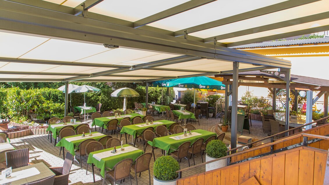 Eine gemütliche Terrasse mit grünen Tischen und Stühlen. Sonnenschirme spenden Schatten in einem einladenden Außenbereich. | © Freiensteinerhof