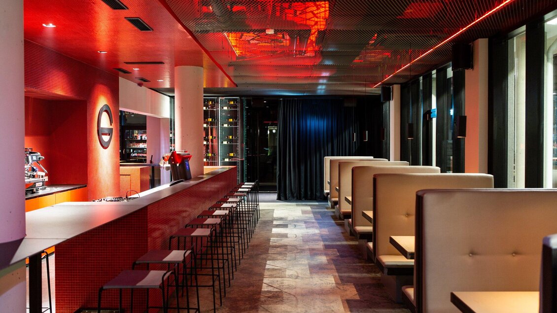 Eine moderne Bar mit roten Akzenten und gemütlichen Sitzecken. Die Lichtverhältnisse schaffen eine einladende Atmosphäre. | © Freigeist