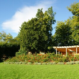 Ein schöner, grüner Garten mit bunten Blumen und einem Holzpavillon. Die Sonne scheint und der Himmel ist blau. | © Franz Grabenhofer
