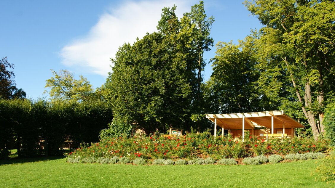 Ein schöner, grüner Garten mit bunten Blumen und einem Holzpavillon. Die Sonne scheint und der Himmel ist blau. | © Franz Grabenhofer