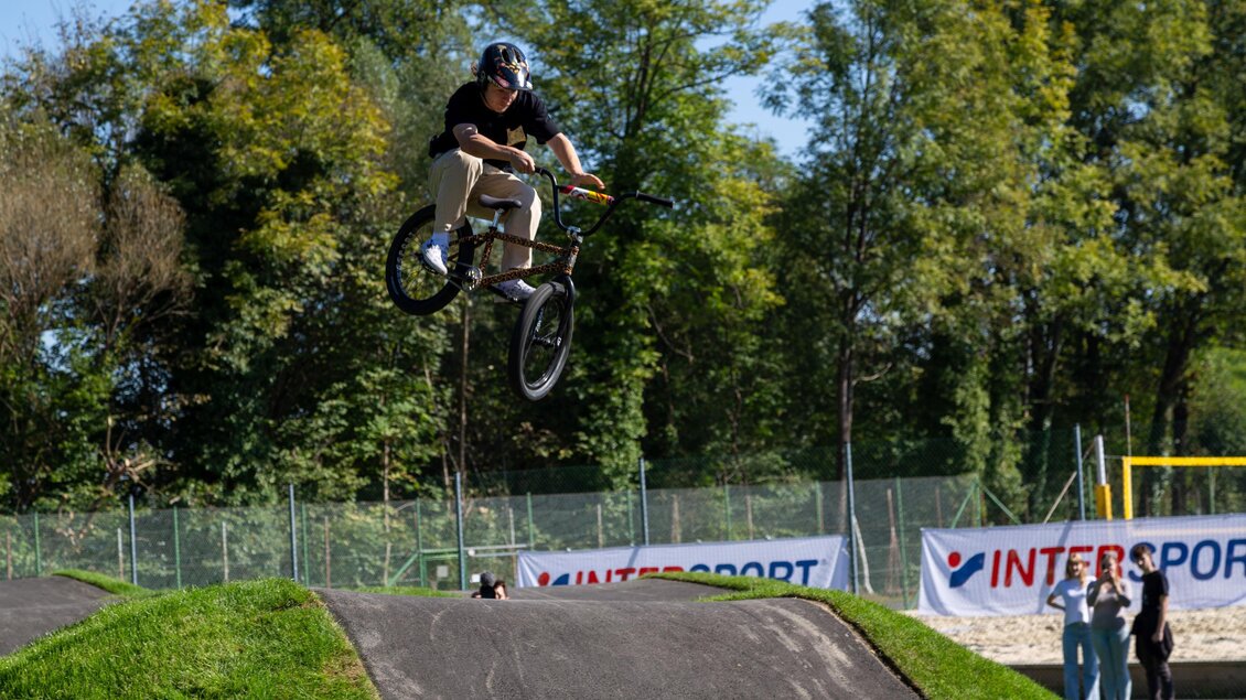 Ein BMX-Fahrer springt über eine Rampe in einem Park. Im Hintergrund sind Zuschauer und eine Werbebande zu sehen. | © Stadtgemeinde Deutschlandsberg | E. Kleindienst