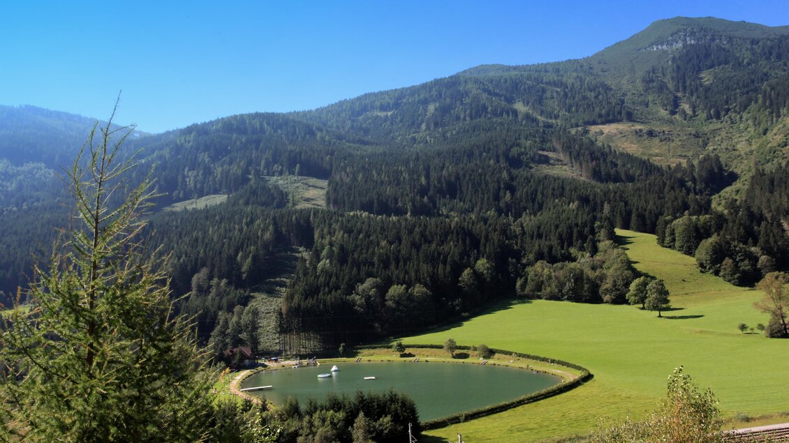 Eine idyllische Landschaft mit sanften Hügeln und dichten Wäldern. Ein kleiner See spiegelt den klaren Himmel wider. | © TVB Erzberg-Leoben