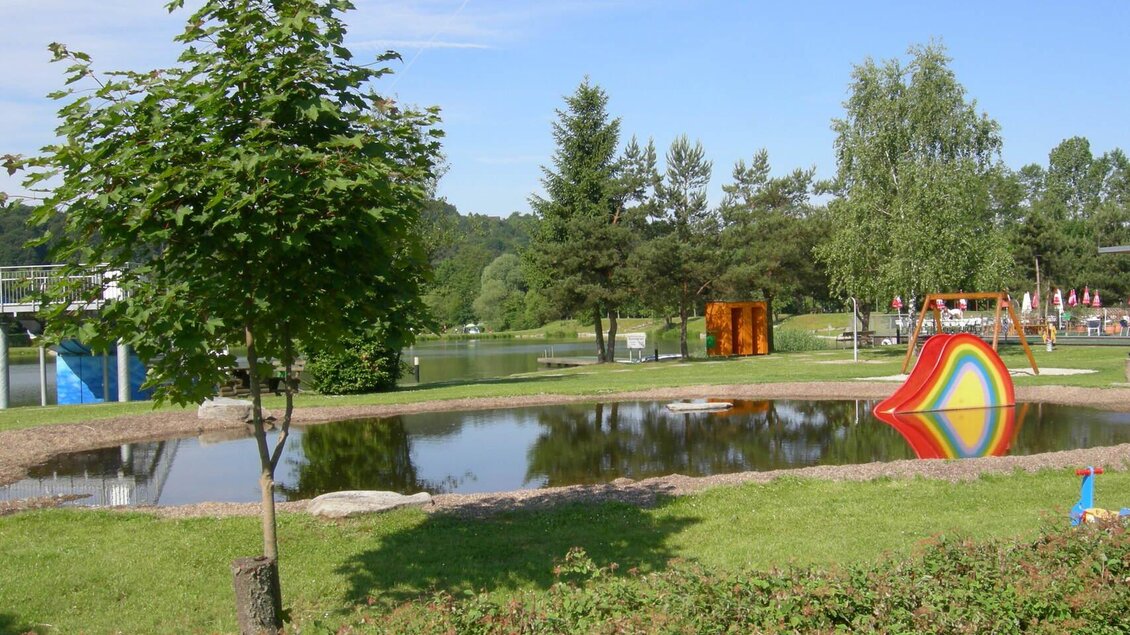 Ein schöner Park mit einem kleinen Teich und bunten Spielgeräten im Hintergrund. Die grüne Landschaft ist ideal für Familien und Kinder. | © Gemeinde Großsteinbach