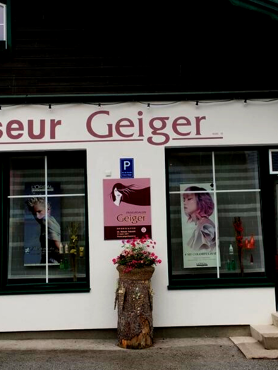 Ein Friseursalon mit dem Namen "Friseur Geiger" an der Fassade. Die Fenster zeigen verschiedene Frisuren und es gibt Blumenschmuck am Eingang. | © Michaela Podsednik